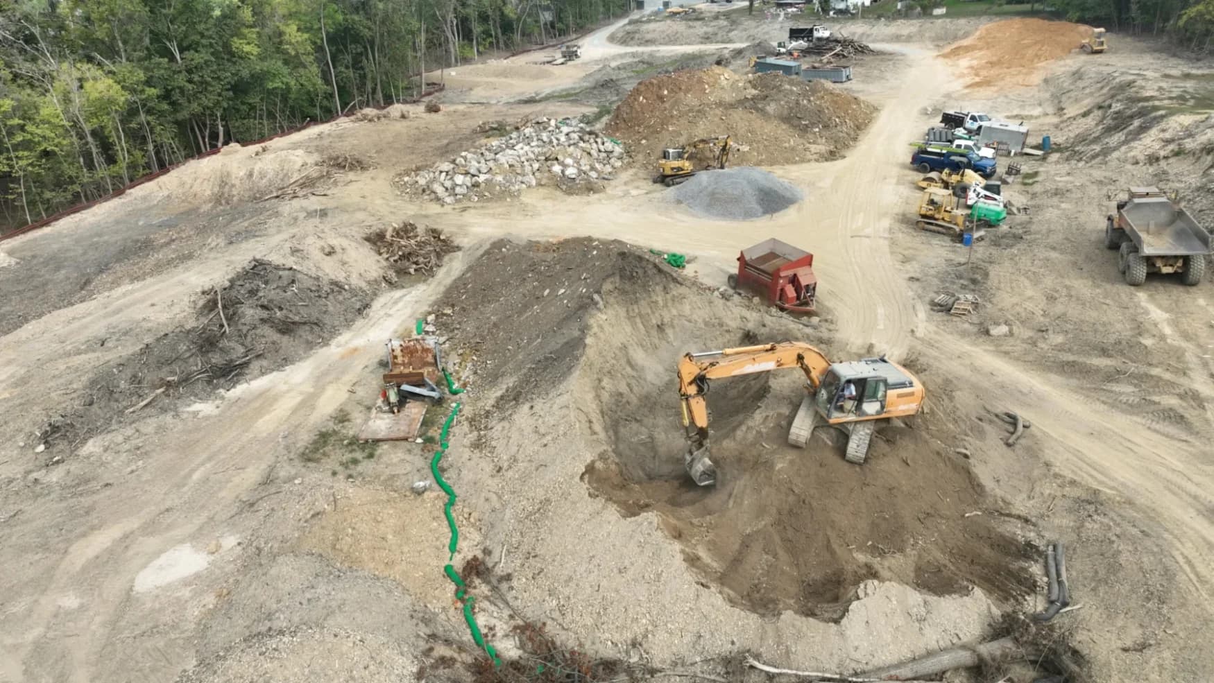 Aerial of a Triple Crown excavation site — an excavator digging beside stone stockpiles and a dump truck